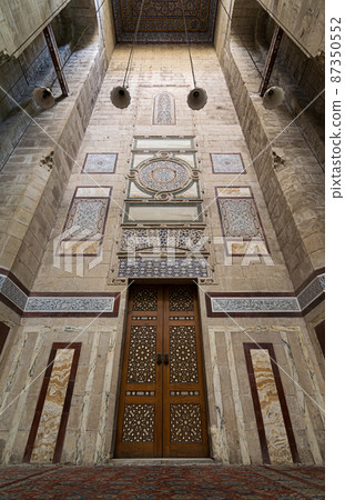 Old decorated stone wall with an ornate wooden door Old decorated stone wall with an ornate wooden door 87350552