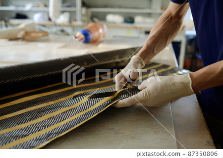 Gloved hands of young manufactory worker cutting special material by workplace Gloved hands of young manufactory worker cutting special material by workplace 87350806