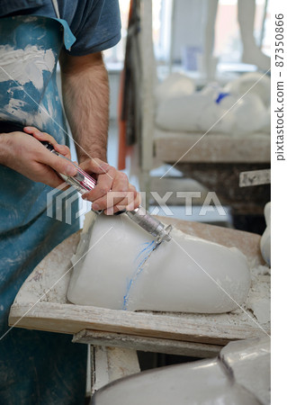 Hands of young manufactory worker cutting part of plaster cast Hands of young manufactory worker cutting part of plaster cast 87350866
