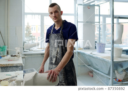 Contemporary young man in apron looking at camera during working process 87350892