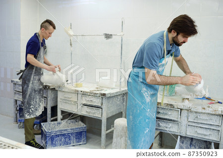 Two young male workers of prosthetic factory standing by tables 87350923