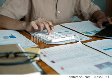 Close up of businesswoman or accountant hand holding pen working on calculator to calculate business data, accountancy document and laptop computer at office, business concept 87351951
