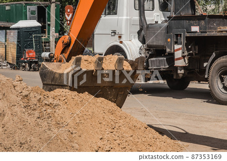 Excavation works. A tractor bucket unloads sand ground with a heavy shovel into a heap against the backdrop of construction site 87353169