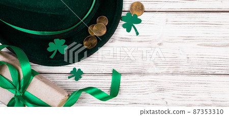 Background for St. Patrick's Day. Leprechaun hat, gold coins and clover shamrock on white wooden background. Good luck symbols. Banner format. Background for St. Patrick's Day. Leprechaun hat, gold coins and clover shamrock on white wooden background. Good luck symbols. Banner format. 87353310