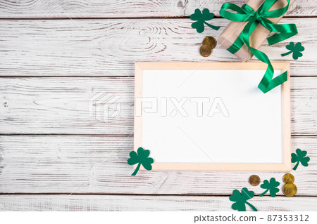 Happy St. Patrick's Day concept. Clover shamrock, gold coins and gift with green ribbon on white background. Festive composition. Place for text. Happy St. Patrick's Day concept. Clover shamrock, gold coins and gift with green ribbon on white background. Festive composition. Place for text. 87353312