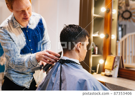 the hairdresser makes a haircut for a man with a hair clipper in a barbershop 87353406
