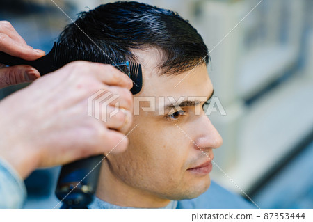 hairdresser makes a haircut of nape for a man with a hair clipper in barbershop 87353444