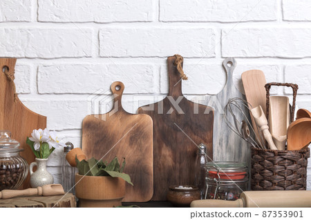 Kitchen utensils and spices on a kitchen countertop against a white brick wall. Food background with wooden eco friendly utensils. Front view 87353901