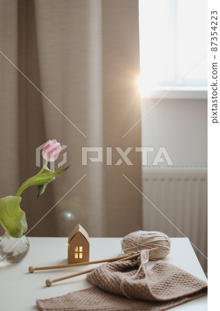 cozy home interior decor with a chair, plaid, table and knitting needles with threads, beige yarn cozy home interior decor with a chair, plaid, table and knitting needles with threads, beige yarn 87354223
