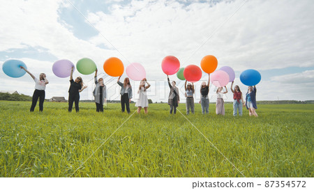 Cheerful girls are standing on the field with large balloons and colorful balloons. 87354572