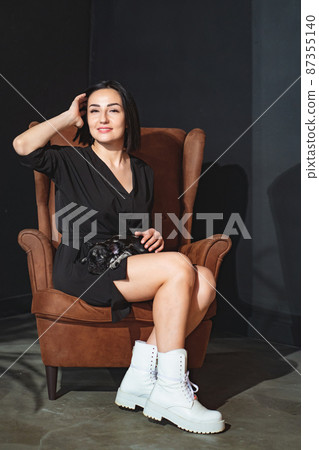 attractive brunette woman with French Bulldog puppy in a brown leather armchair 87355140