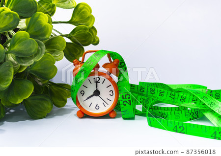 Measure tap with orange clock on white wooden background. Diet concept. Measure tap with orange clock on white wooden background. Diet concept. 87356018
