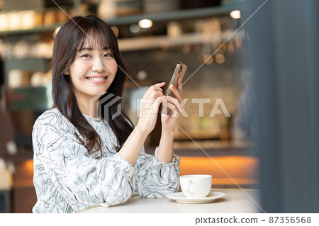 A young woman operating a smartphone in a cafe A young woman operating a smartphone in a cafe 87356568