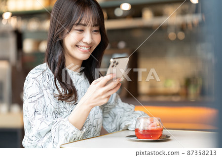 一位年輕女子在咖啡館喝茶時看智能手機 87358213
