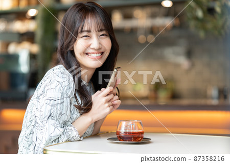 A young woman watching a smartphone while drinking tea at a cafe A young woman watching a smartphone while drinking tea at a cafe 87358216