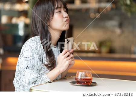 A young woman watching a smartphone while drinking tea at a cafe A young woman watching a smartphone while drinking tea at a cafe 87358218