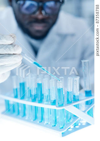 Close-up of scientist in protective wear pouring the liquid in test tubes with pipette during work in laboratory Close-up of scientist in protective wear pouring the liquid in test tubes with pipette during work in laboratory 87358788