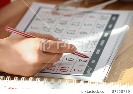 Woman marking date in calendar at wooden table, closeup Woman marking date in calendar at wooden table, closeup 87358789