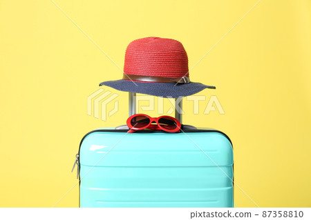 Turquoise suitcase with sunglasses and hat on yellow background 87358810