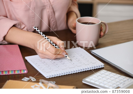 Woman marking date in calendar at wooden table, closeup 87359008