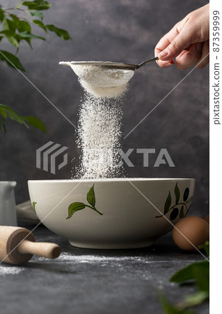 Woman's hand sifting flour through sieve. Selective focus. Baking, cooking, pastry abstract concept. Dark background 87359999