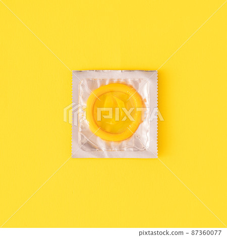 Yellow condom in transparent package on yellow background 87360077