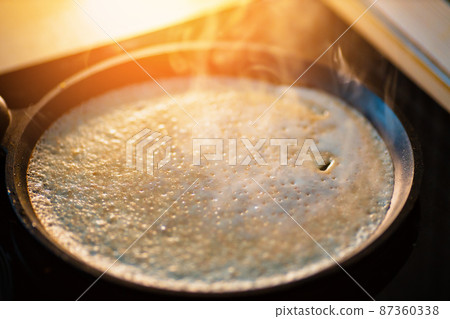 Pancake is baked in black cast iron skillet and there is smoke. Preparation of delicious traditional Pancake is baked in black cast iron skillet and there is smoke. Preparation of delicious traditional 87360338