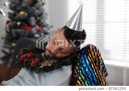 Drunk man with festive cap and wreath sleeping in room after New Year party Drunk man with festive cap and wreath sleeping in room after New Year party 87361293