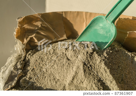 Grey sand-concrete dry mix in an open paper bag. Concrete dry powder for leveling walls and floors. Repair in the house with your own hands. DIY. Selective focus Grey sand-concrete dry mix in an open paper bag. Concrete dry powder for leveling walls and floors. Repair in the house with your own hands. DIY. Selective focus 87361907