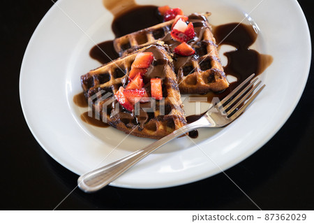 Waffles with chocolate syrup and strawberries 87362029