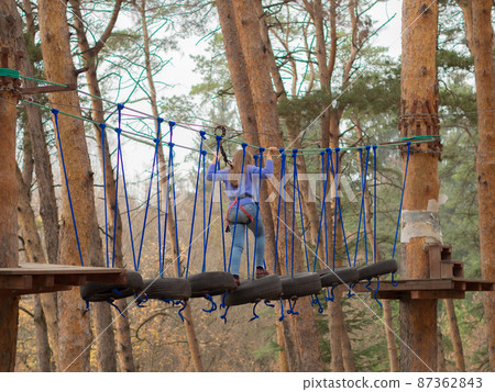 A girl walks along a suspension bridge made of car wheels and ropes. Extreme entertainment for children. Rope park A girl walks along a suspension bridge made of car wheels and ropes. Extreme entertainment for children. Rope park 87362843