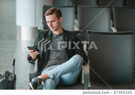 Passenger in an airport lounge waiting for flight aircraft. Young man with smartphone in airport waiting for landing Passenger in an airport lounge waiting for flight aircraft. Young man with smartphone in airport waiting for landing 87363184