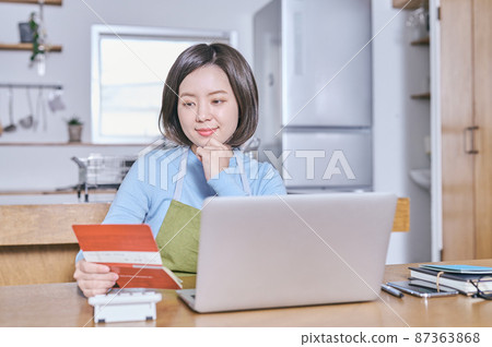 A young woman in an apron looking at her bankbook with a smile 87363868