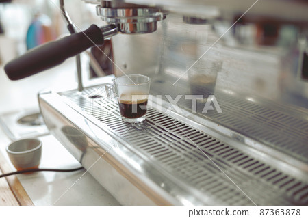 Close up of glass cup with coffee standing on grate of coffee machine 87363878