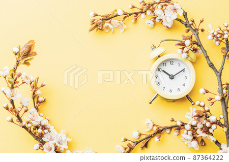 Spring time background. May flowers and April floral nature with alarm clock on yellow. Branches of blossoming apricot macro with soft focus. For easter greeting cards with copy space. Springtime. 87364222