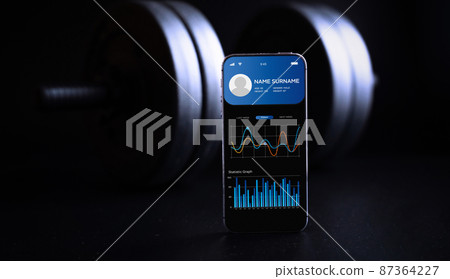 Gym application. Smart phone screen with fitness health or sport gym mobile application on black dumbbell background. Online fitness program. Gym application. Smart phone screen with fitness health or sport gym mobile application on black dumbbell background. Online fitness program. 87364227