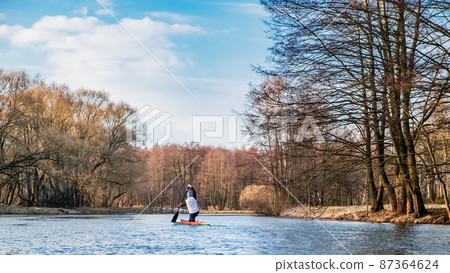 A lone paddler sails down the river in a canoe in early spring A lone paddler sails down the river in a canoe in early spring 87364624