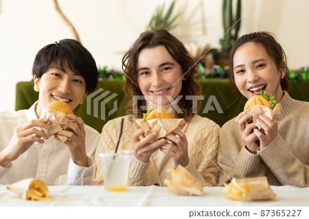 Young men and women eating hamburgers in the room Young men and women eating hamburgers in the room 87365227