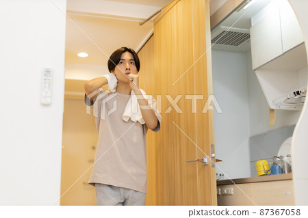 Young man drying his hair while brushing his teeth Young man drying his hair while brushing his teeth 87367058