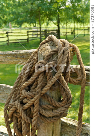 Thick Coiled Manila Rope Hanging over a Wooden Fencepost in a Rural Ranch Setting in Summer Thick Coiled Manila Rope Hanging over a Wooden Fencepost in a Rural Ranch Setting in Summer 87370595