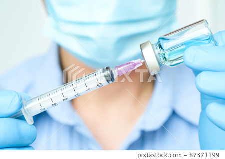 doctor's hand holds a syringe and a blue vaccine bottle at the hospital. Health and medical concepts. doctor's hand holds a syringe and a blue vaccine bottle at the hospital. Health and medical concepts. 87371199