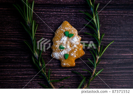 Cookies in the form of a Christmas tree, sprinkled with powdered sugar and small Christmas trees on top, lies on a dark wooden background surrounded by grained rosemary. High quality photo Cookies in the form of a Christmas tree, sprinkled with powdered sugar and small Christmas trees on top, lies on a dark wooden background surrounded by grained rosemary. High quality photo 87371552