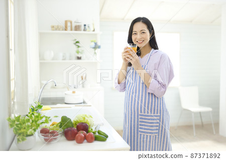 Pregnant woman drinking orange jeice in the kitchen Pregnant woman drinking orange jeice in the kitchen 87371892