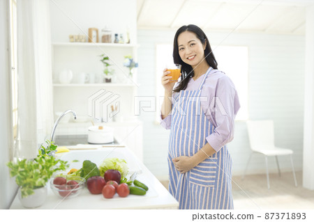 Pregnant woman drinking orange jeice in the kitchen Pregnant woman drinking orange jeice in the kitchen 87371893
