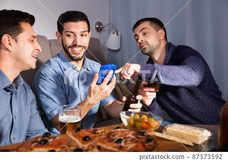 Male friends sitting with phone at home 87373592