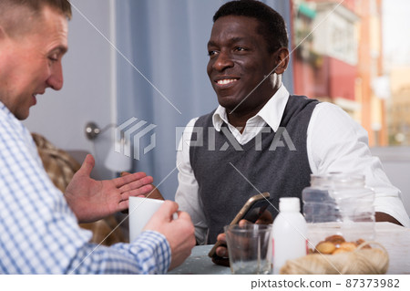 Positive male friends using mobile, talking in home interior 87373982