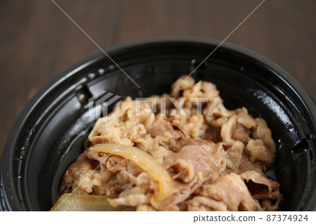 木桌上黑色塑料容器中的 Gyudon 87374924