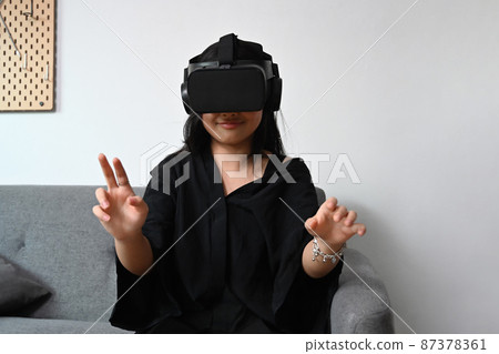 Exited asian girl wearing virtual reality headset to watching video or play video game and touch something on the air. 87378361