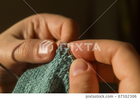 Close-up hand knitting. Hobbies, handicrafts. Knitting warm clothes from woolen fine yarn by hand on metal needles. Selective focus Close-up hand knitting. Hobbies, handicrafts. Knitting warm clothes from woolen fine yarn by hand on metal needles. Selective focus 87382306