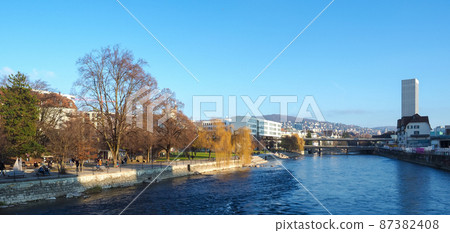 Zurich, Switzerland - December 18th 2021: People enjoying autumnal colours and sunlight in a park at the Limmat river 87382408